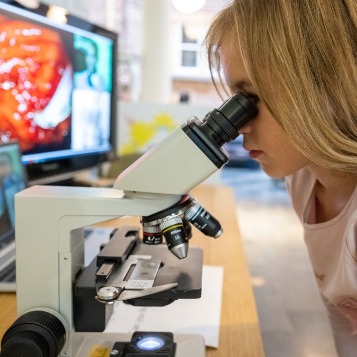 Jonge deelneemster kijkt door microscoop